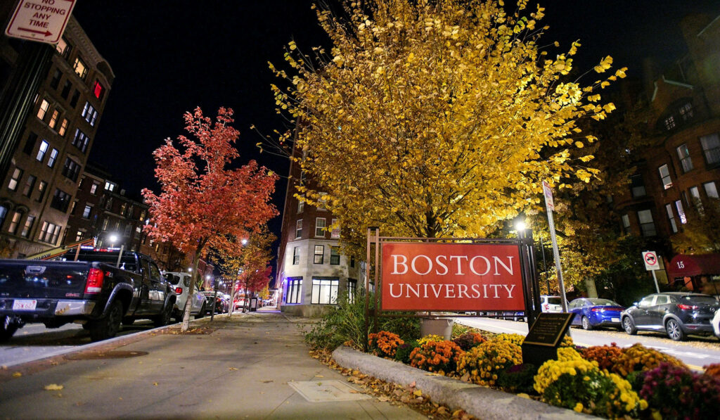 Boston University sign illuminated at night with autumn trees and historic brick buildings background Wallpaper