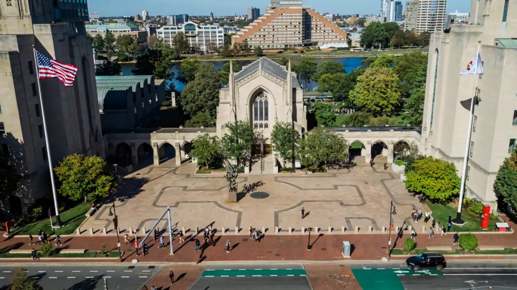 Boston University Theology Department neo-Gothic building with greenery and cityscape under blue sky Wallpaper