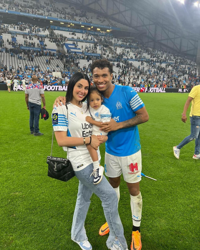 Boubacar Kamara with wife Coralie Porrovecchio and baby celebrating on vibrant football field with fans Wallpaper