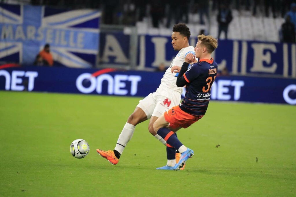 Boubacar Kamara controlling ball in intense football match with Marseille banner and stadium lights Wallpaper