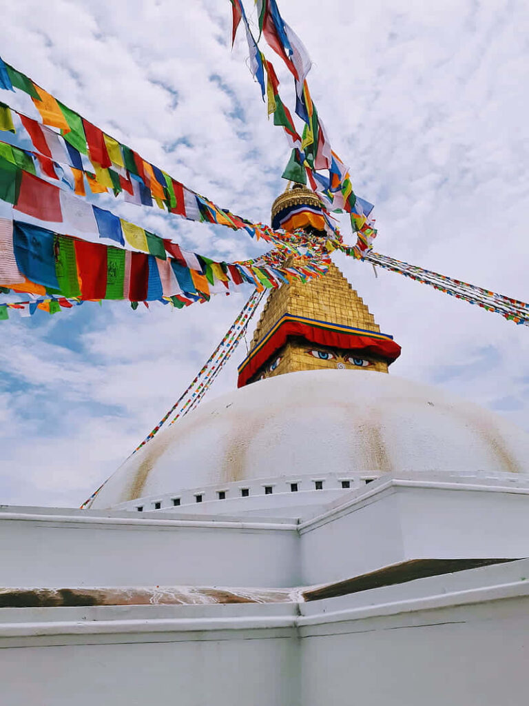 Boudhanath Stupa side view with colorful prayer flags golden spire bright blue sky Kathmandu Nepal Wallpaper