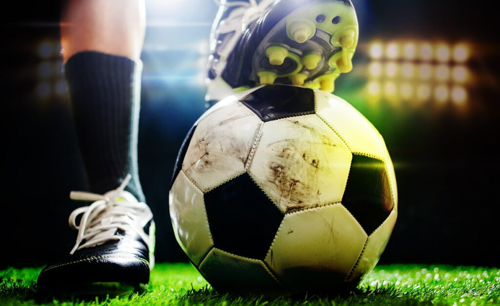 Close-up of classic black and white soccer ball under cleated boot with stadium lighting background Wallpaper