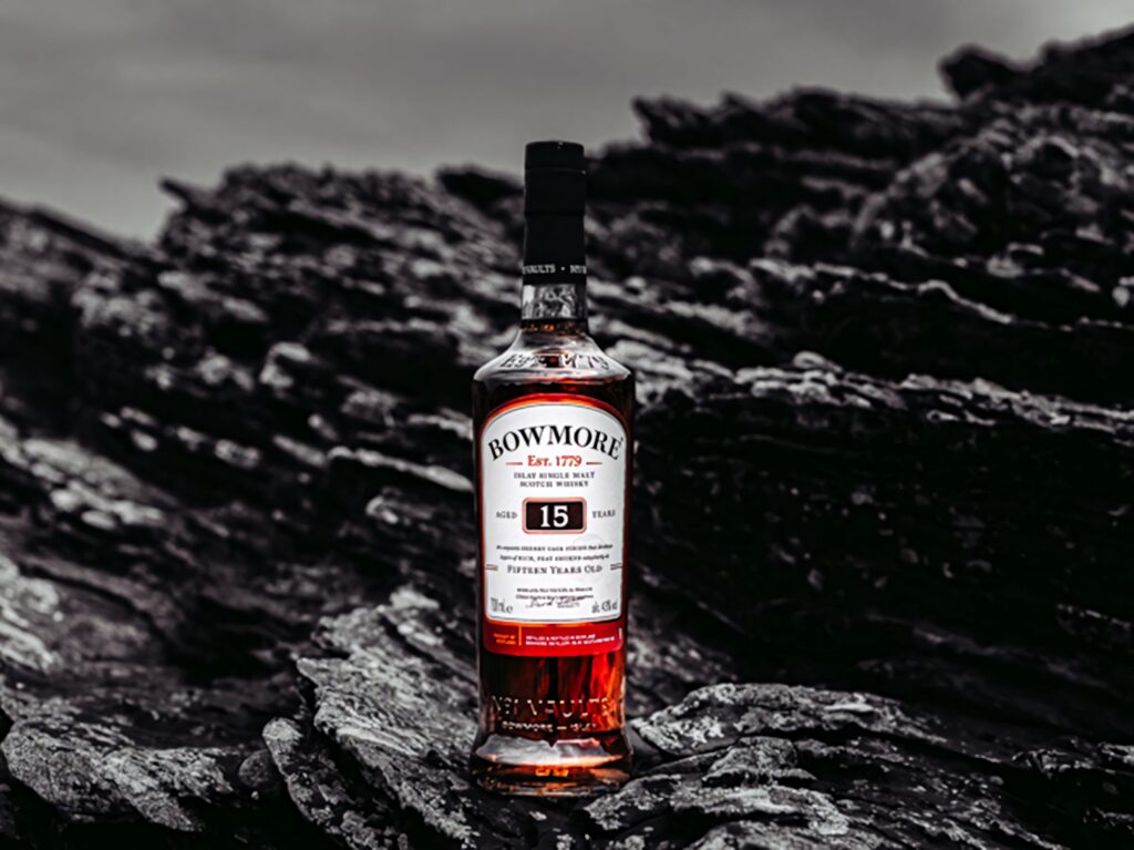 Bowmore 15 Year Old Scotch Whisky bottle on dark rugged rocks with rich amber whiskey color Wallpaper
