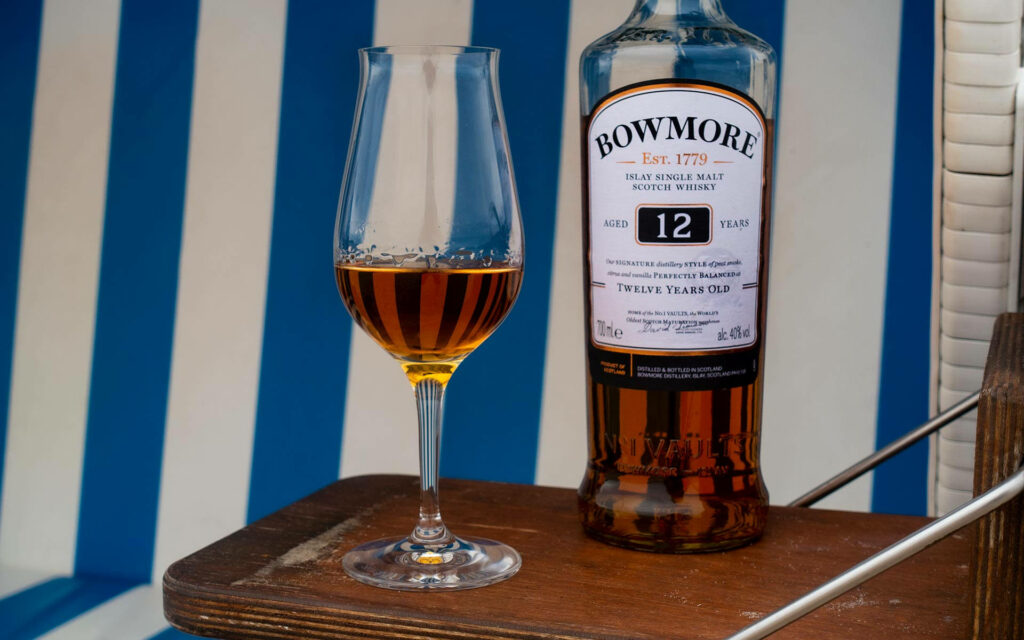 Close-up of Bowmore 12 Years Old whisky glass and bottle on blue striped background wallpaper