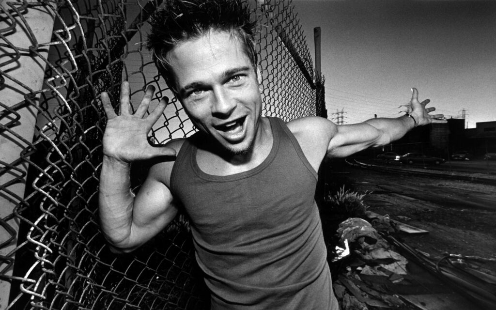 Brad Pitt playful pose by chain-link fence during dramatic sunset vibrant wallpaper background
