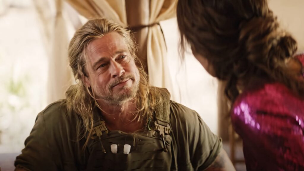Brad Pitt in rugged outfit with long hair talking to woman in vibrant The Lost City movie scene Wallpaper