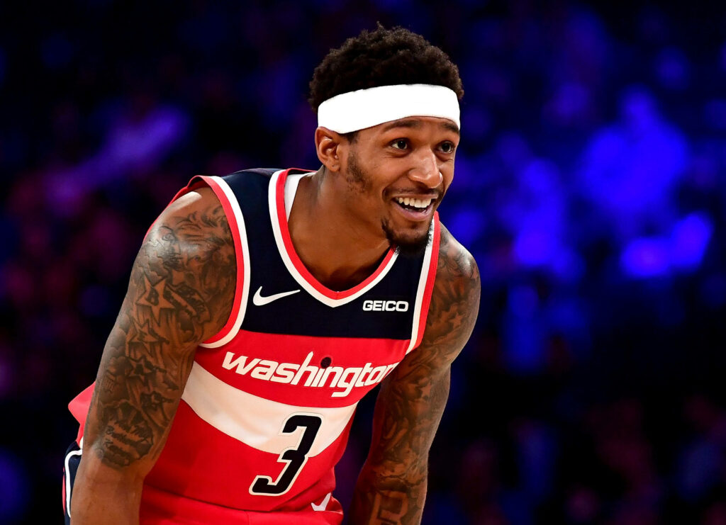Bradley Beal smiling mid-game in Washington Wizards jersey with vibrant arena lights background Wallpaper