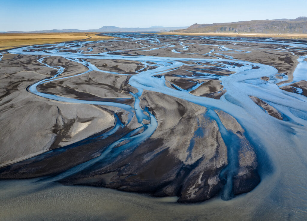 Braided river with blue streams flowing across dark sandy shores in rugged wilderness wallpaper