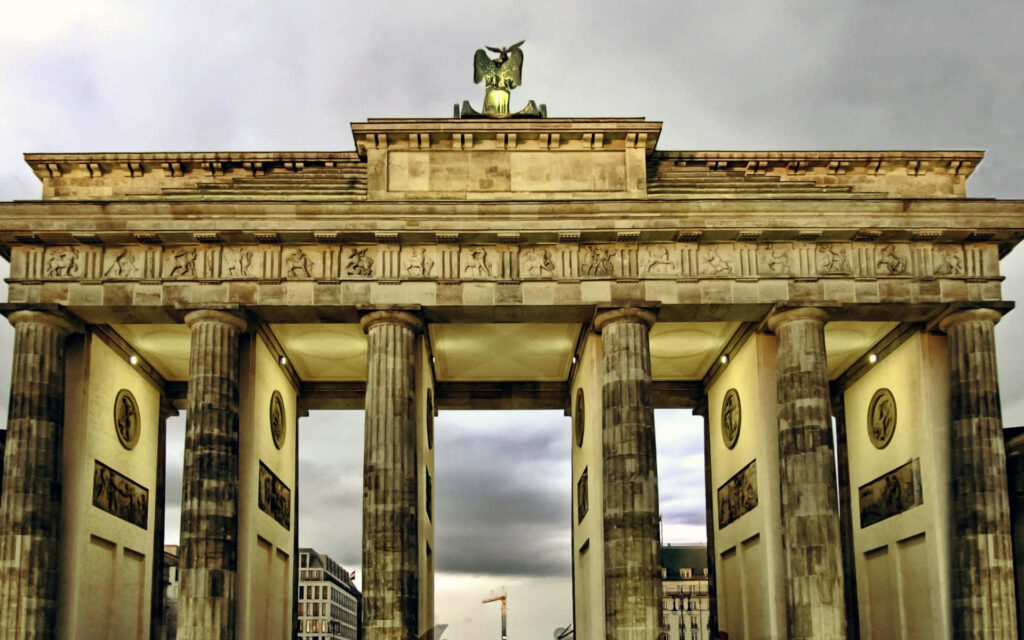 Brandenburg Gate illuminated at night with dramatic clouds and detailed historic architecture Wallpaper