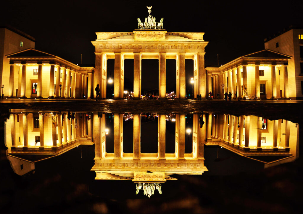 Night view of Brandenburg Gate illuminated with golden lights reflected in calm water wallpaper