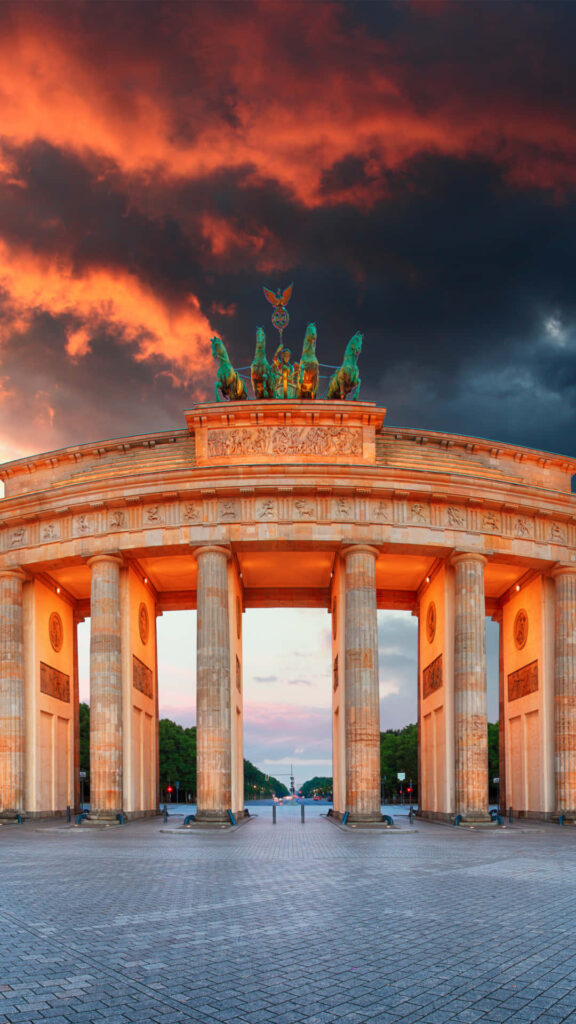 Brandenburg Gate illuminated at sunset with dramatic orange sky and neoclassical architecture Wallpaper