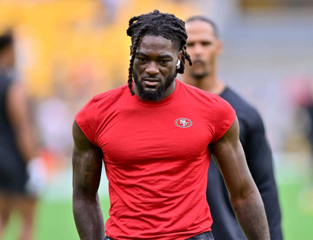 Brandon Aiyuk 49ers focused in red shirt during pre game warmup with blurred stadium background Wallpaper