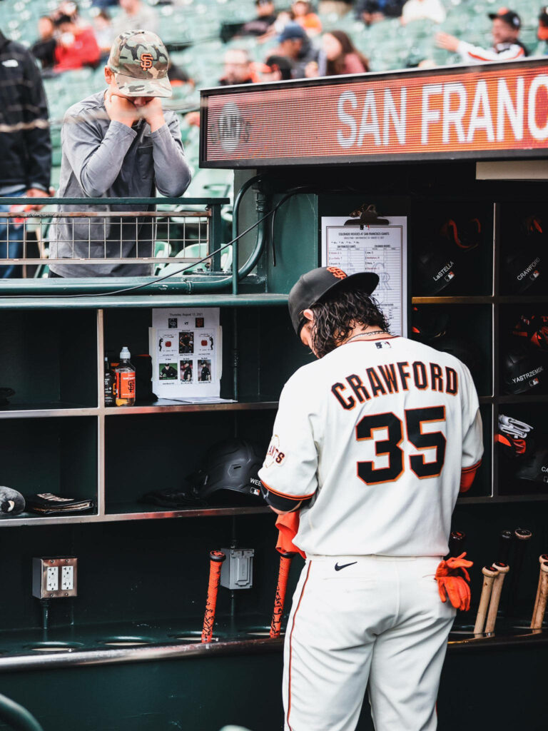 Brandon Crawford in white Giants jersey number 35 organizing gear in vibrant dugout before game Wallpaper