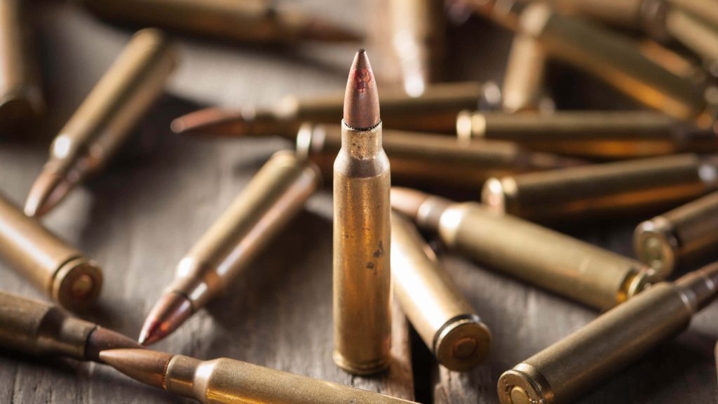 Macro shot of a brass rifle cartridge standing on wood with blurred bullets in warm light background Wallpaper