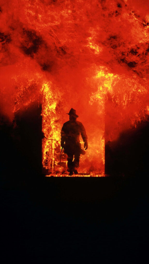 Firefighter standing strong amid towering flames inside burning building intense inferno wallpaper
