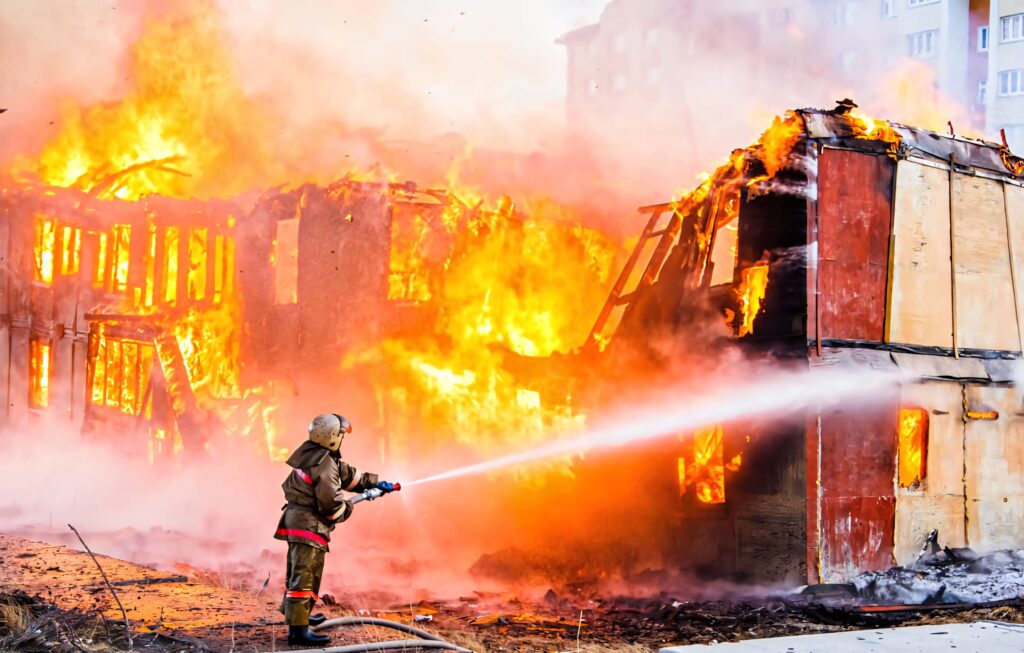 Fire department officer battling intense flames and thick smoke at burning building complex wallpaper