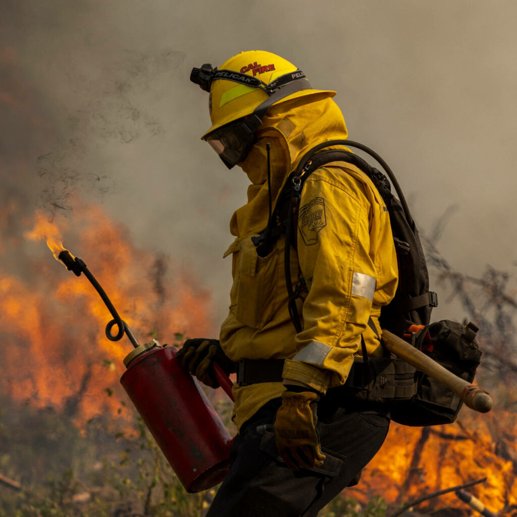 Firefighter in yellow gear with suppression equipment battling intense forest fire smoke background Wallpaper