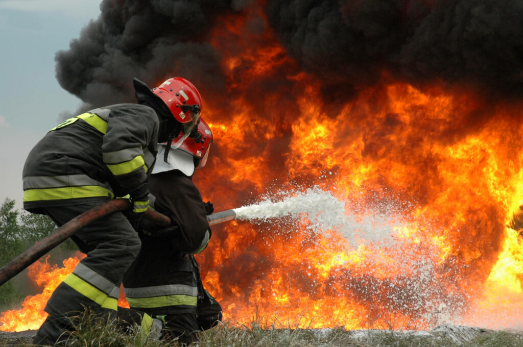 Firefighters in protective gear battling intense blaze with water stream and thick smoke wallpaper