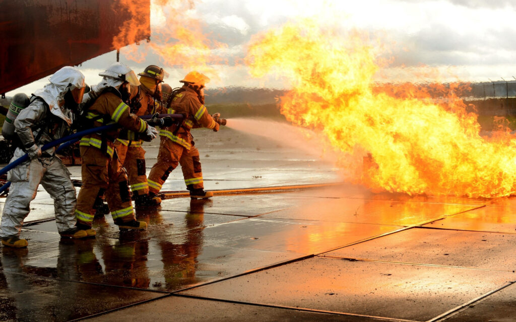 Firefighters battling intense flames with water hoses showing teamwork bravery wallpaper