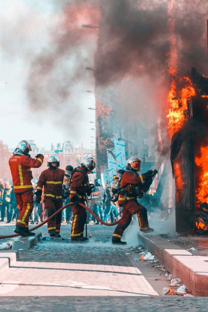 Firefighters in protective gear battling fierce industrial fire with heavy smoke in urban area Wallpaper