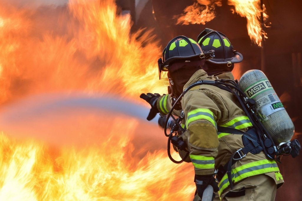 Firefighters in full gear battling massive blazing fire in intense high contrast action scene wallpaper
