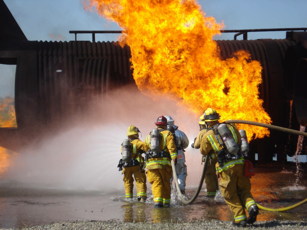 Firefighters in full gear battling intense flames and smoke showing teamwork and bravery Wallpaper