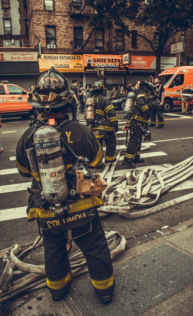 Brave firefighters in full gear working on city street with hoses and emergency vehicles wallpaper
