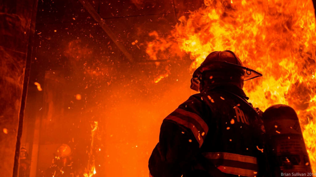 Fireman standing bravely amid raging intense flames showing courage and resilience wallpaper