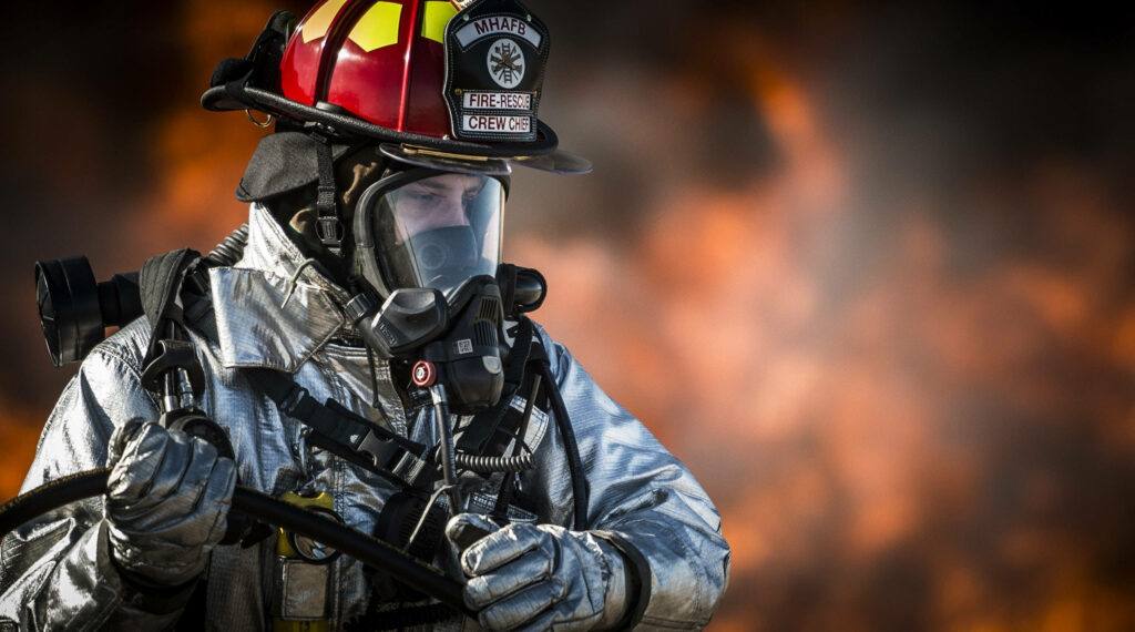Fireman in full gear holding hose amid intense flames showing bravery and dedication wallpaper