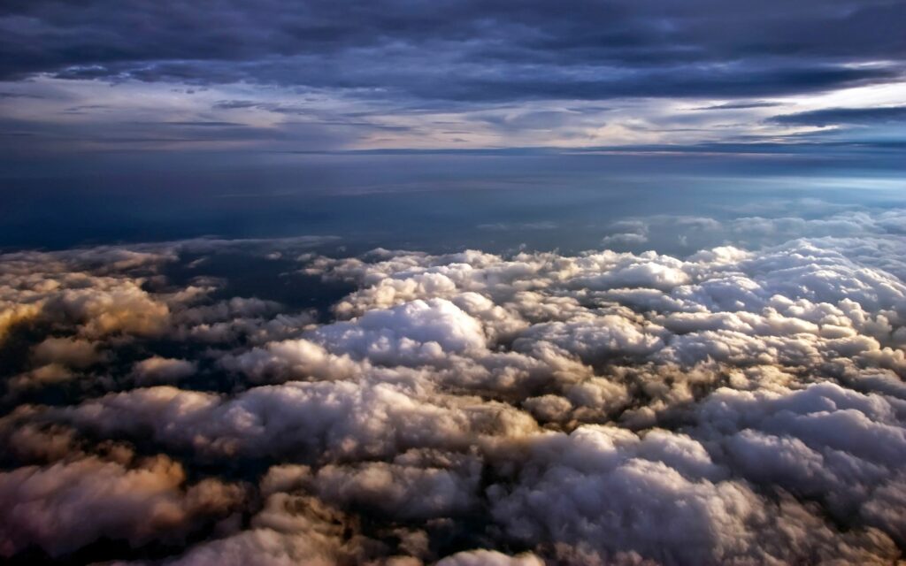 Aerial view of soft clouds under dramatic sky with blue gray tones and warm sunlight wallpaper