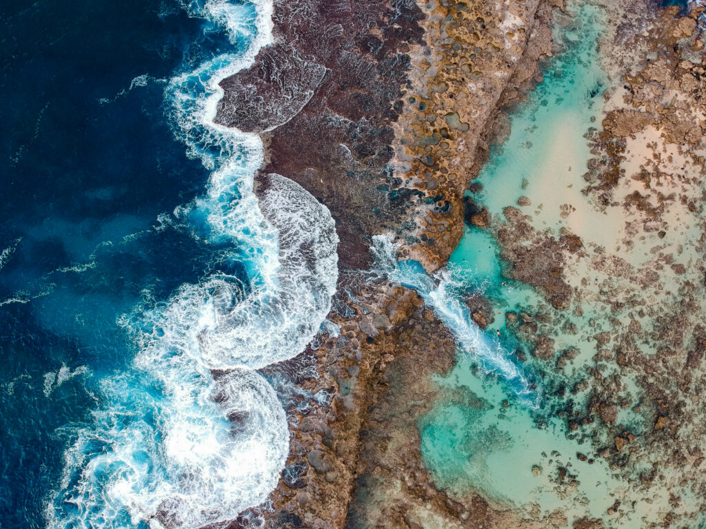 Aerial view of Hawaiian shore with turquoise waters rugged rocks and foamy ocean surf wallpaper