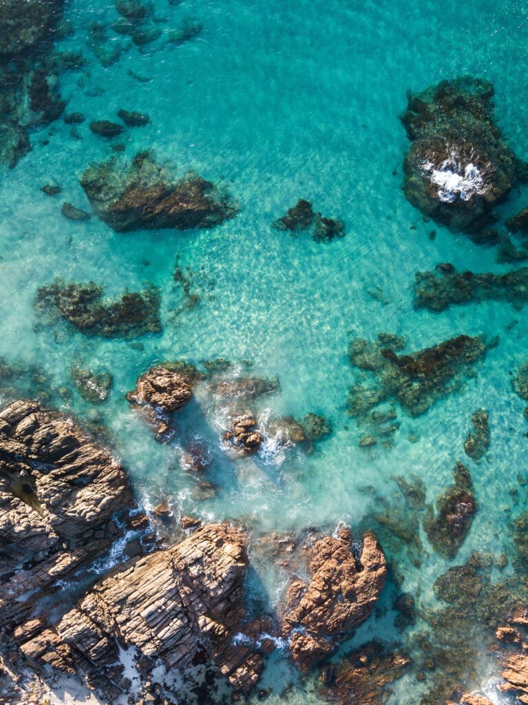 Aerial view of rugged rocks and turquoise sea with gentle surf on textured shoreline wallpaper