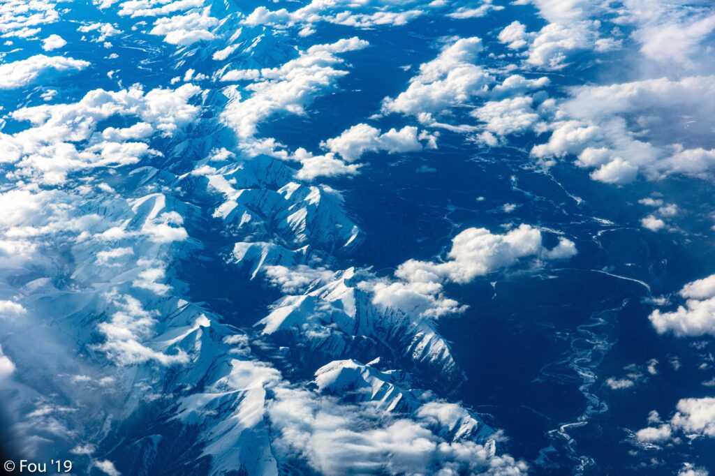 Aerial view of snow-capped mountains with clouds and winding blue rivers vibrant wallpaper background