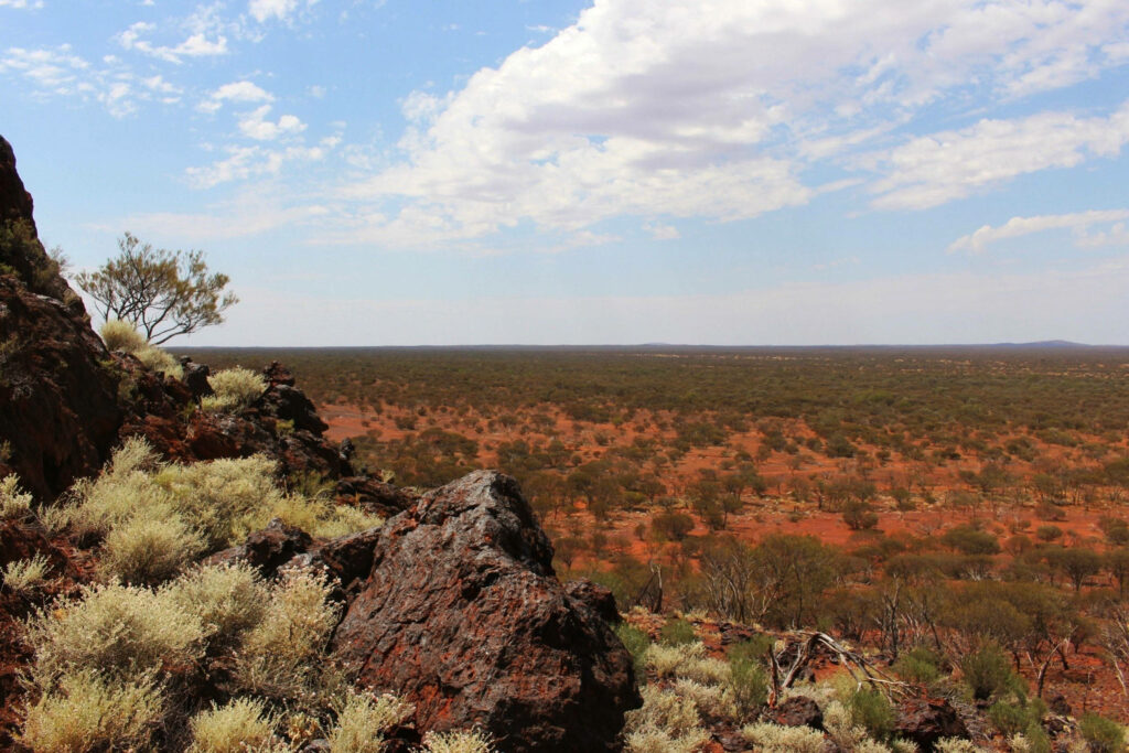 Vast Australian Outback landscape with rugged rocks native shrubs and red earth under cloudy sky Wallpaper