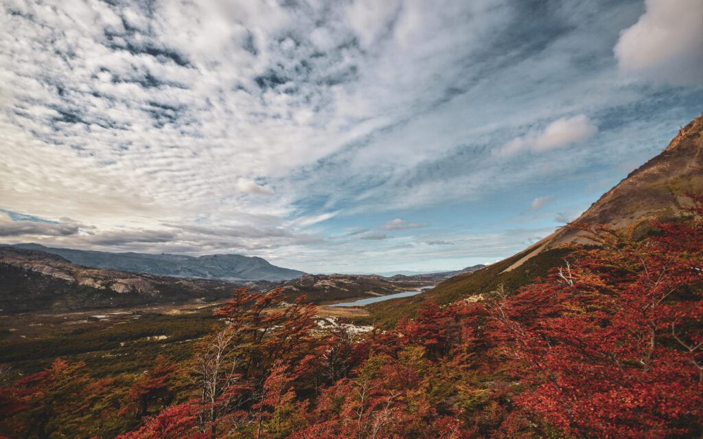 Autumn landscape wallpaper with vibrant red trees majestic mountains and dynamic cloudy sky