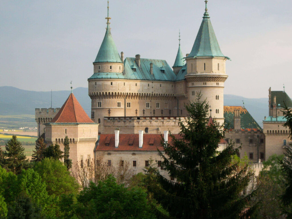 Bojnice Castle vibrant rooftops fairytale spires medieval architecture lush greenery mountains Wallpaper