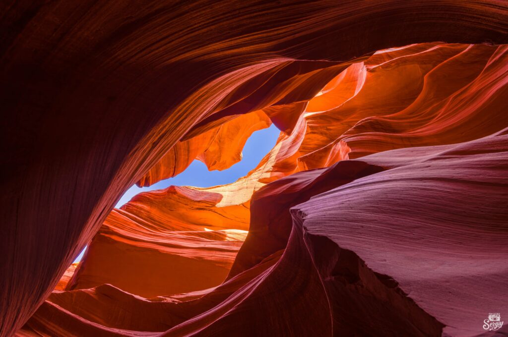 Bottom view of vibrant orange red canyon rock formations under vivid blue sky wallpaper background