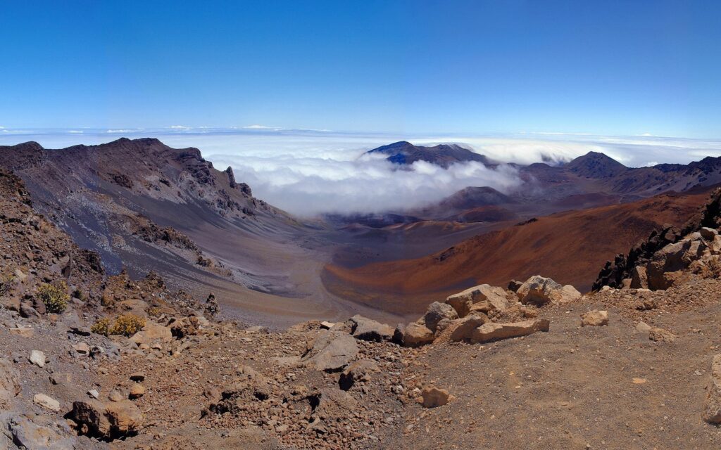 Breathtaking canyon with rocky slopes and billowing clouds under a clear blue sky wallpaper