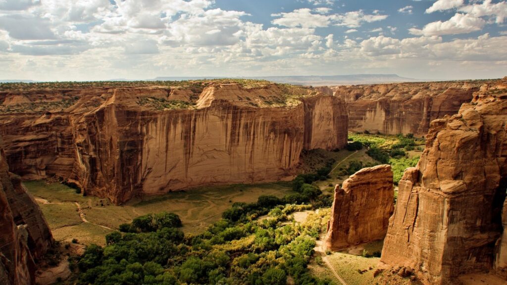 Breathtaking canyon landscape with towering cliffs lush greenery and dramatic cloudy sky background Wallpaper