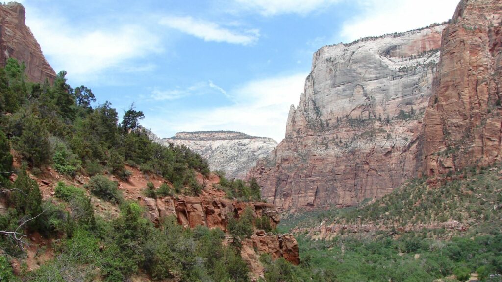 Breathtaking canyon landscape with towering red rock walls lush greenery and bright blue sky Wallpaper