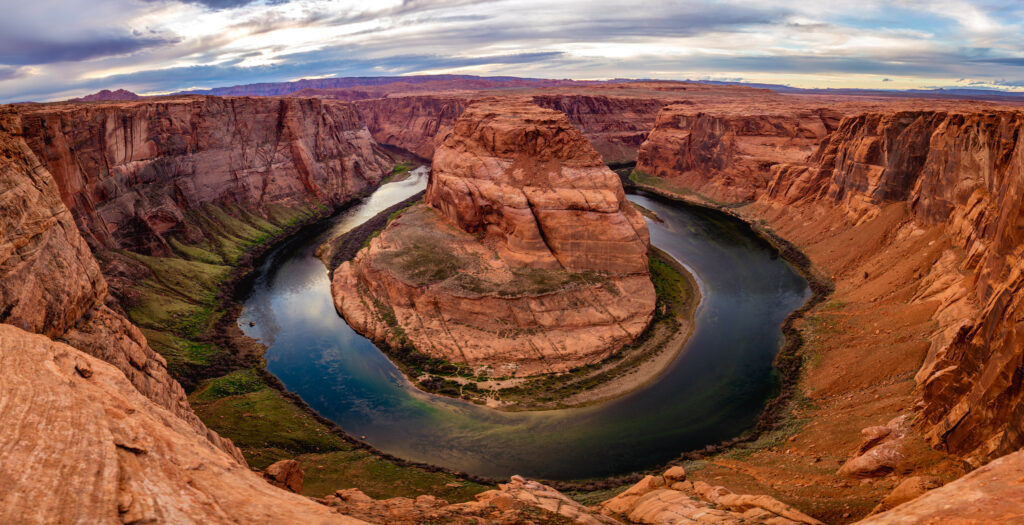 Vast canyon with rugged red rocks and winding river under dramatic sky showcasing nature beauty Wallpaper