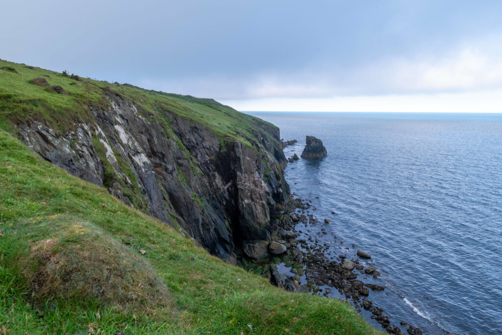 Cliffside view with rugged rocks lush green grass serene sea scattered stones misty horizon wallpaper