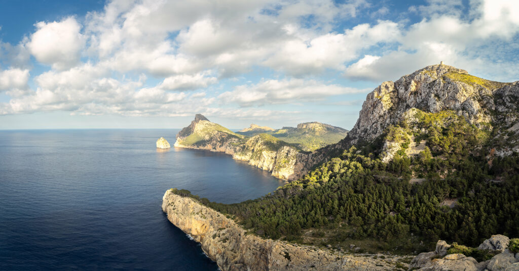 Breathtaking coastal landscape with rugged rocks green forests and deep blue sea under cloudy sky Wallpaper