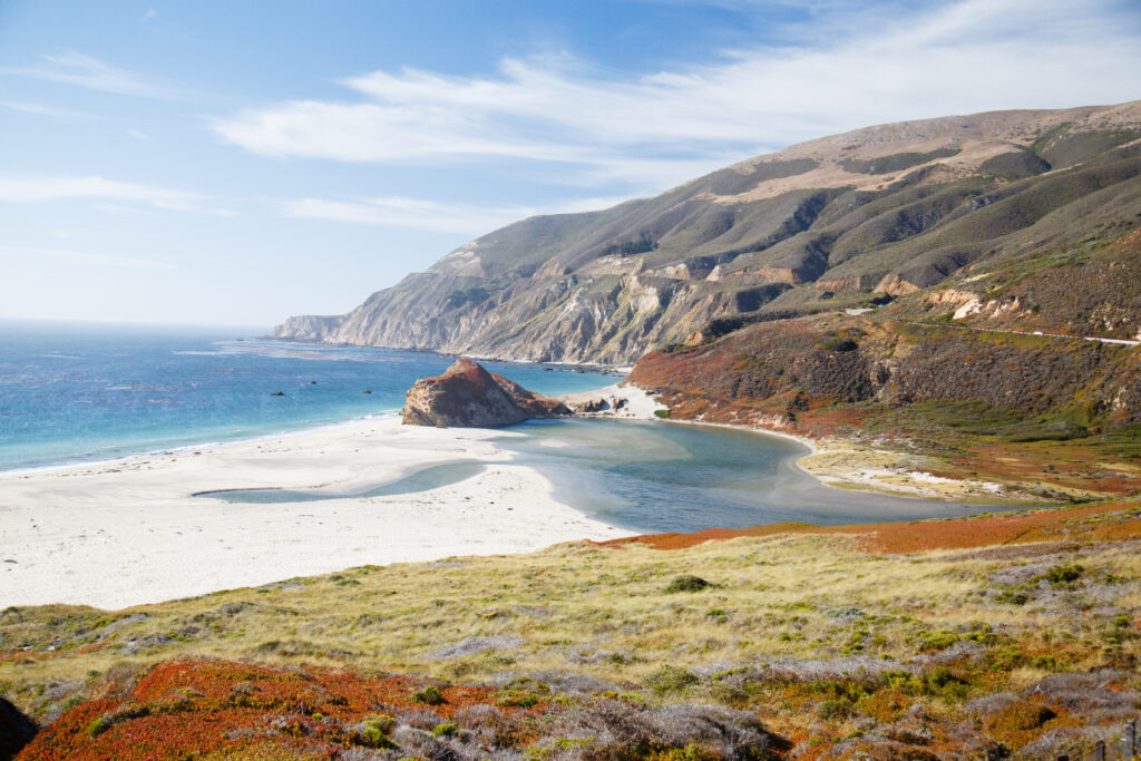 Coastal landscape wallpaper with rugged mountains vivid blue sea sandy shore and lush vegetation