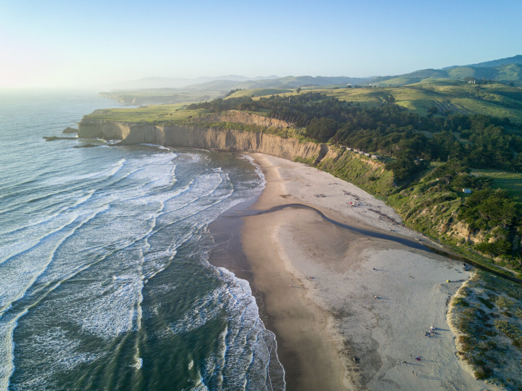 Coastal landscape wallpaper with sandy beach waves rocky shore cliffs and green hills under blue sky
