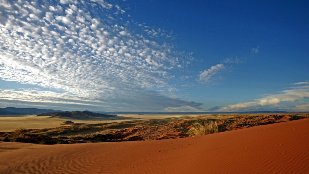 Vast desert landscape with red sand dunes and dramatic textured clouds under open sky wallpaper
