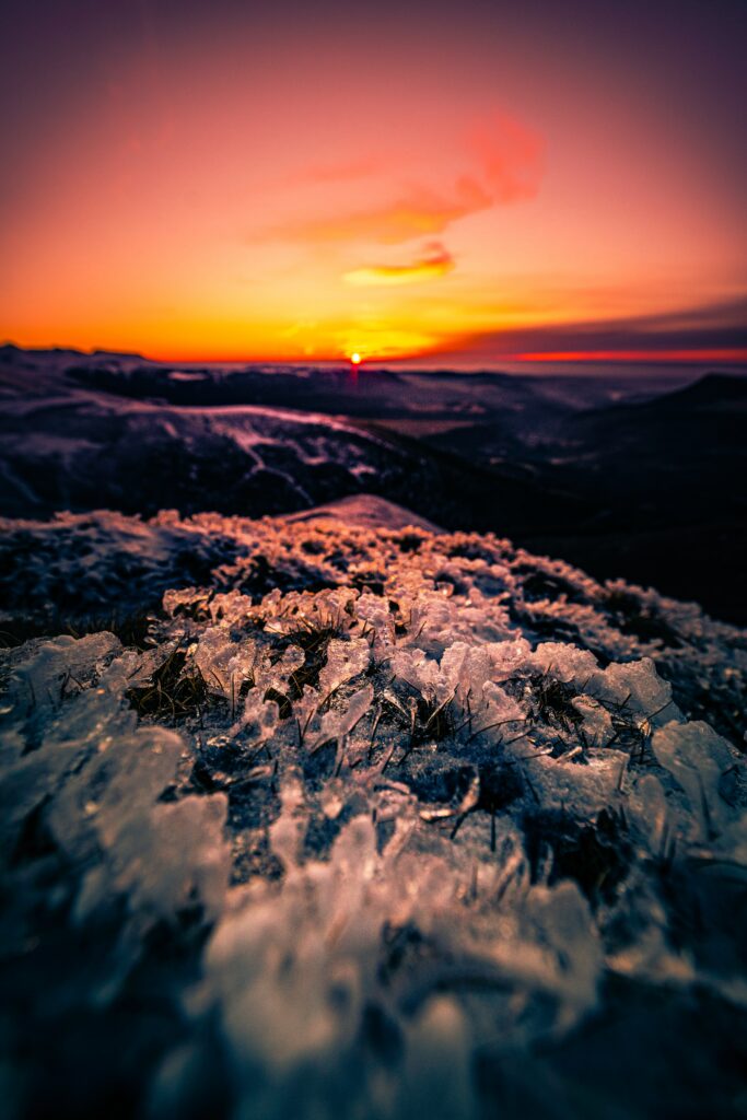 Breathtaking sunset over frozen landscape with ice formations on grass and rocks wallpaper background