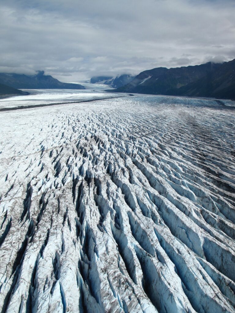 Breathtaking glacier landscape with deep blue ice fissures and distant mountains under clouds Wallpaper