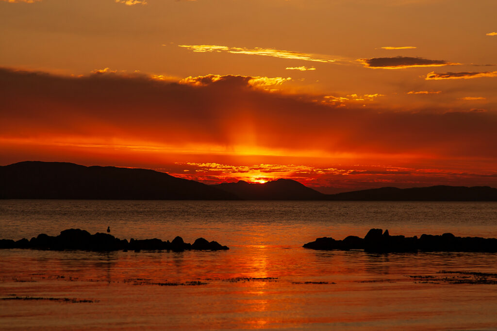 Sunset over sea with golden orange sky silhouetted stones calm water reflection serene wallpaper