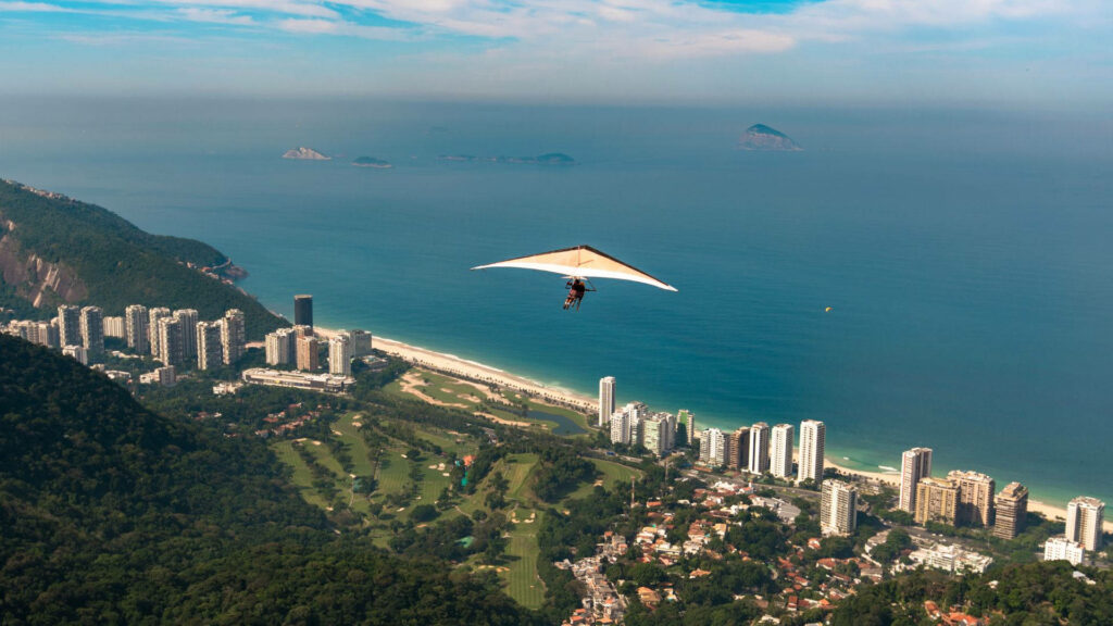 Hang Glider Soars Over Stunning Beach and Lush Green Landscape Wallpaper